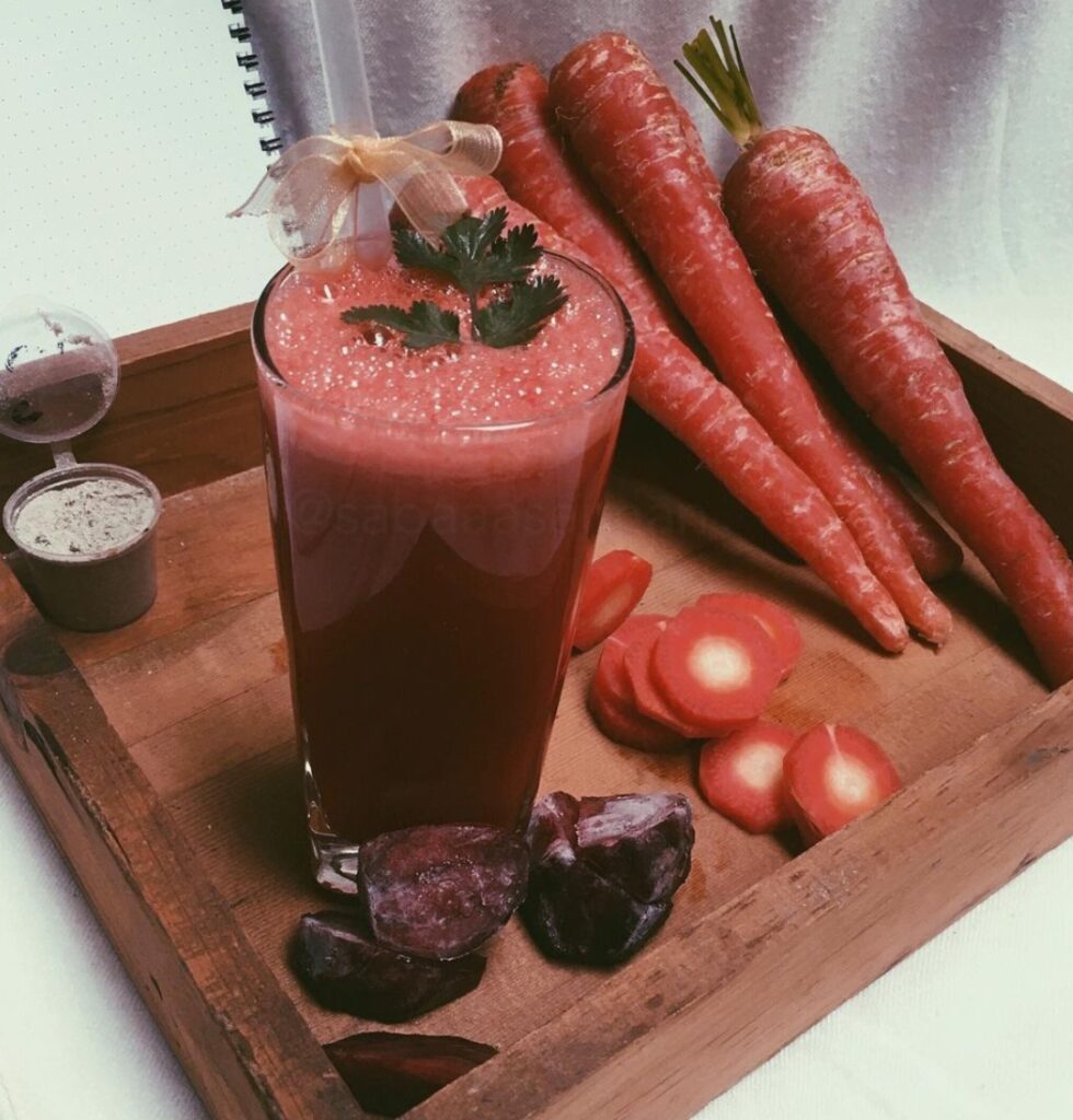 a glass of juice next to carrots