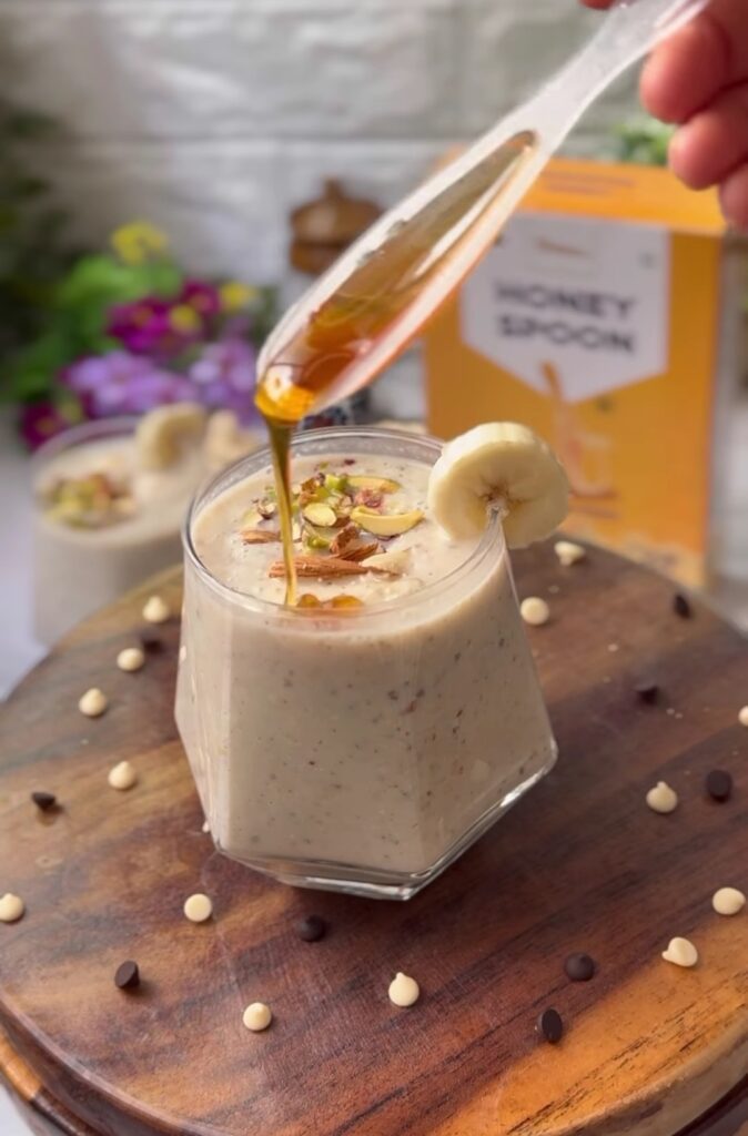 a glass of milk with a banana and nuts on a wooden surface